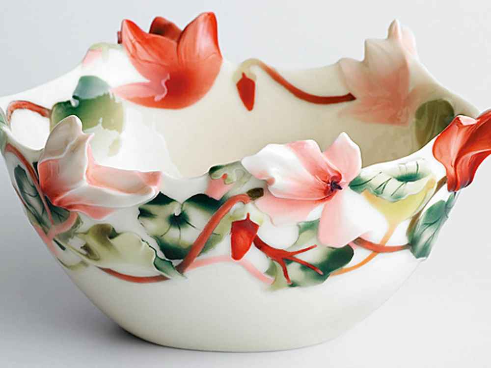 White porcelain bowl with a scalloped rim and sculpted red and pink cyclamen flowers